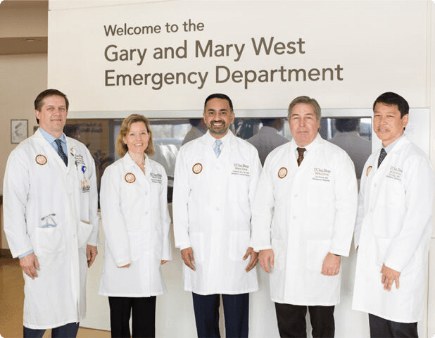 Five medical professionals in white coats stand in front of a sign for the Gary and Mary West Emergency Department.